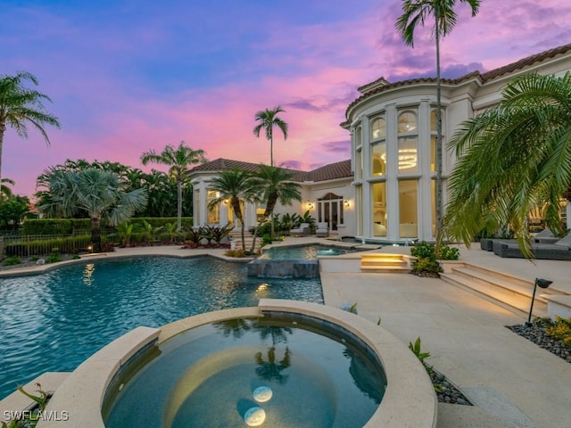 pool at dusk with an in ground hot tub