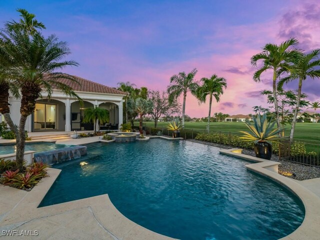 pool at dusk with pool water feature and an in ground hot tub