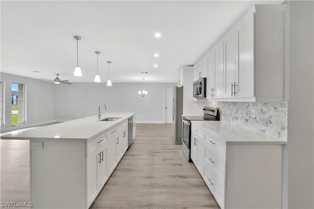 kitchen featuring an island with sink, white cabinets, appliances with stainless steel finishes, light hardwood / wood-style floors, and ceiling fan with notable chandelier