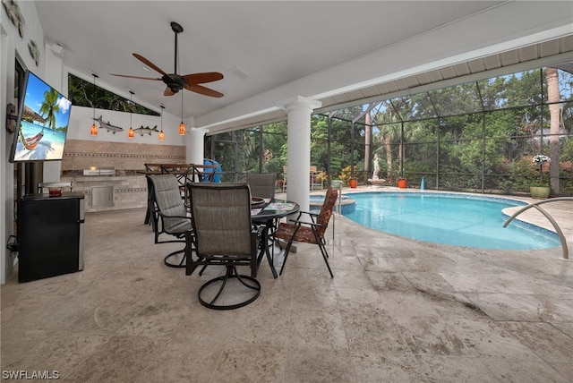 view of pool with glass enclosure, ceiling fan, exterior kitchen, and a patio