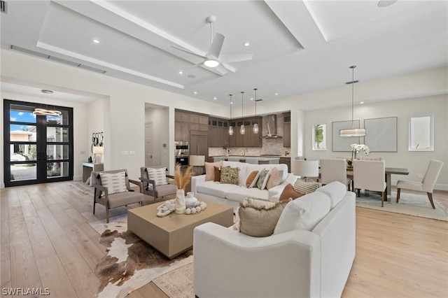 living room with light hardwood / wood-style floors, french doors, a tray ceiling, and ceiling fan