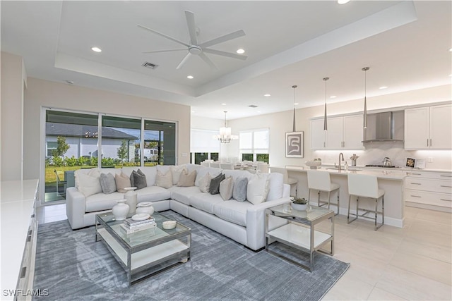 tiled living room featuring ceiling fan with notable chandelier, a tray ceiling, and sink