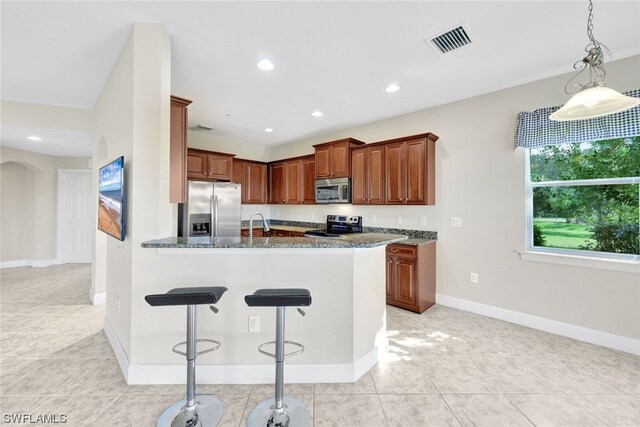 kitchen featuring dark stone counters, stainless steel appliances, pendant lighting, kitchen peninsula, and light tile patterned floors