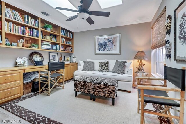 carpeted home office featuring ornamental molding, built in desk, ceiling fan, and a skylight