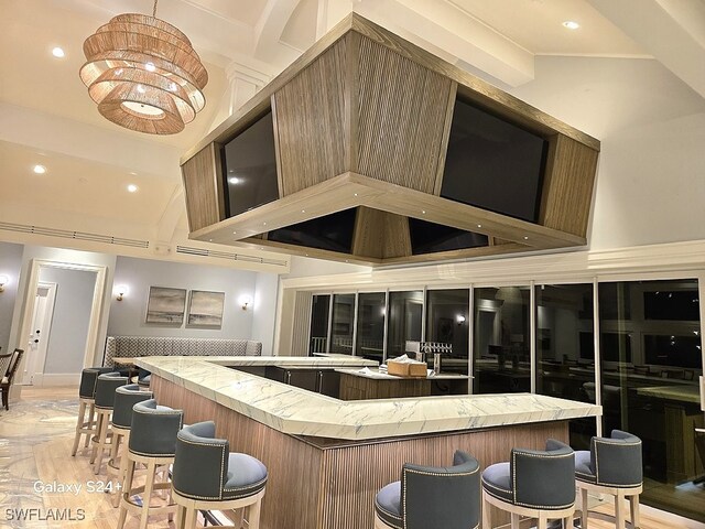 bar with a chandelier, high vaulted ceiling, and wall chimney range hood