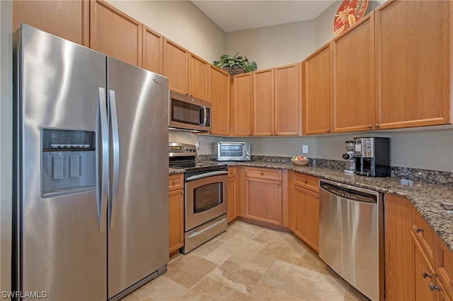 kitchen with stainless steel appliances, light tile floors, and dark stone countertops