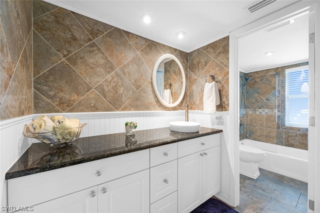 full bathroom featuring tile walls, vanity with extensive cabinet space, toilet, tiled shower / bath, and tile flooring