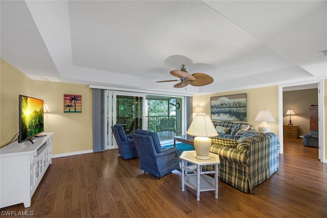 living room with dark wood-type flooring, ceiling fan, and a tray ceiling