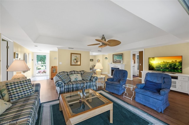 living room with dark hardwood / wood-style floors, ceiling fan, and a tray ceiling