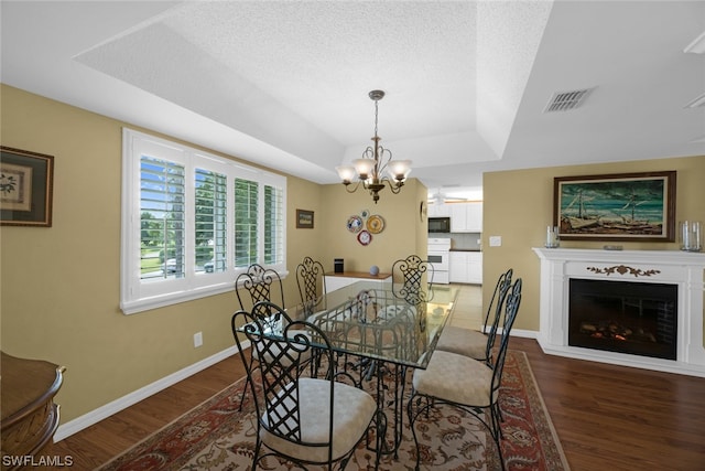 dining space with a chandelier, dark wood-type flooring, and a raised ceiling