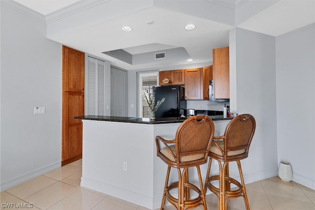 kitchen with light tile floors, kitchen peninsula, a breakfast bar area, a raised ceiling, and black fridge