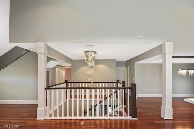 corridor with baseboards, wood finished floors, a notable chandelier, and an upstairs landing