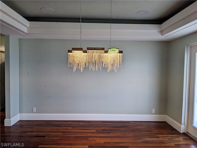 unfurnished dining area with a tray ceiling, a notable chandelier, baseboards, and wood finished floors