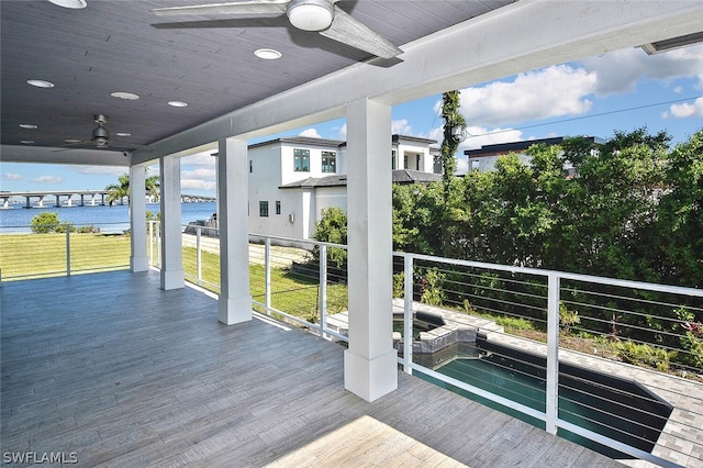 deck with a water view, ceiling fan, and an in ground hot tub