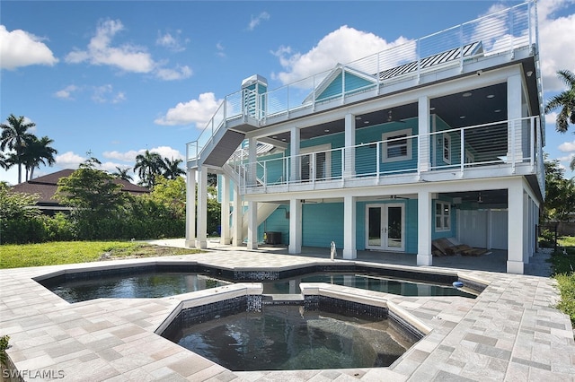 rear view of property with a swimming pool with hot tub, a balcony, a patio area, and french doors