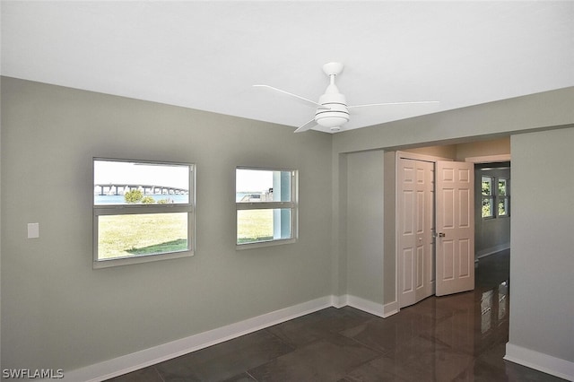 empty room with ceiling fan, dark tile patterned flooring, a wealth of natural light, and baseboards