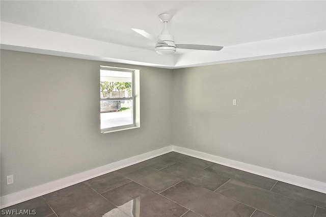 unfurnished room featuring dark tile patterned floors, a ceiling fan, and baseboards