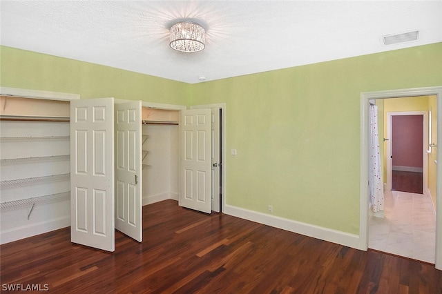 unfurnished bedroom featuring multiple closets, visible vents, baseboards, and wood finished floors