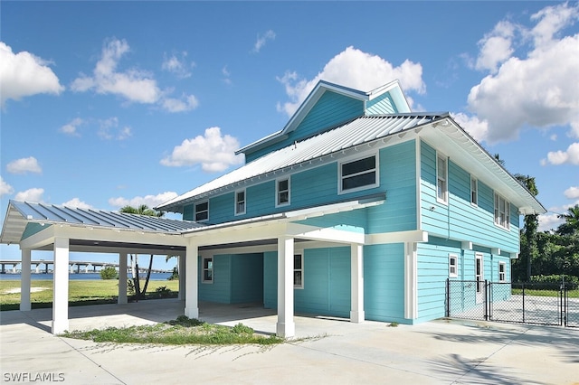 view of front facade with a standing seam roof, a gate, metal roof, fence, and a carport