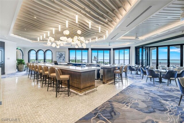 bar with a water view, a raised ceiling, a notable chandelier, and tile patterned flooring