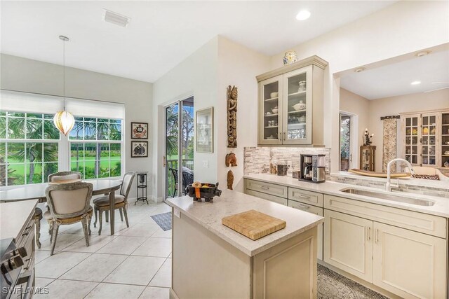 kitchen with decorative backsplash, sink, light tile patterned flooring, hanging light fixtures, and cream cabinetry