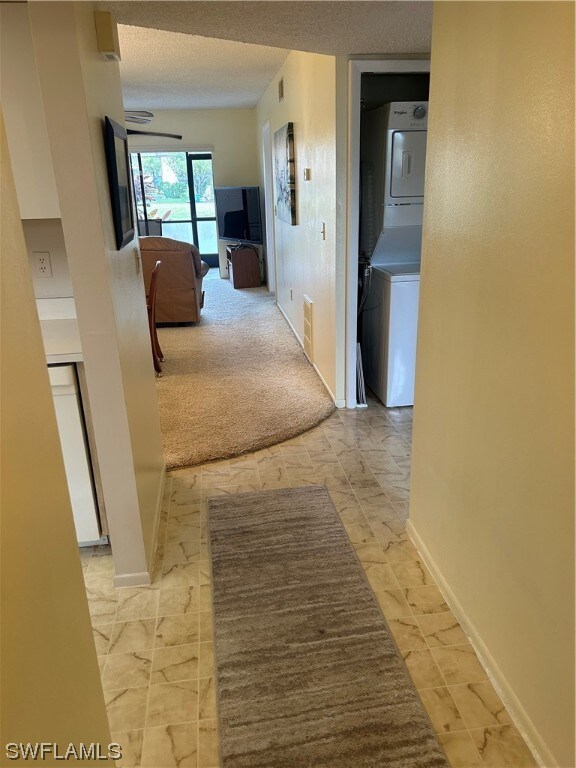 corridor featuring stacked washer / drying machine, light tile floors, and a textured ceiling