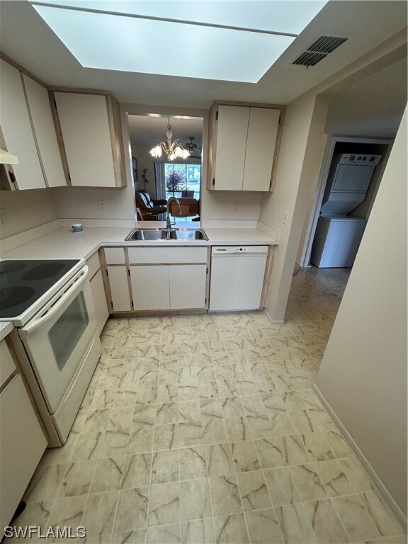 kitchen with white appliances, sink, light tile floors, a skylight, and a notable chandelier