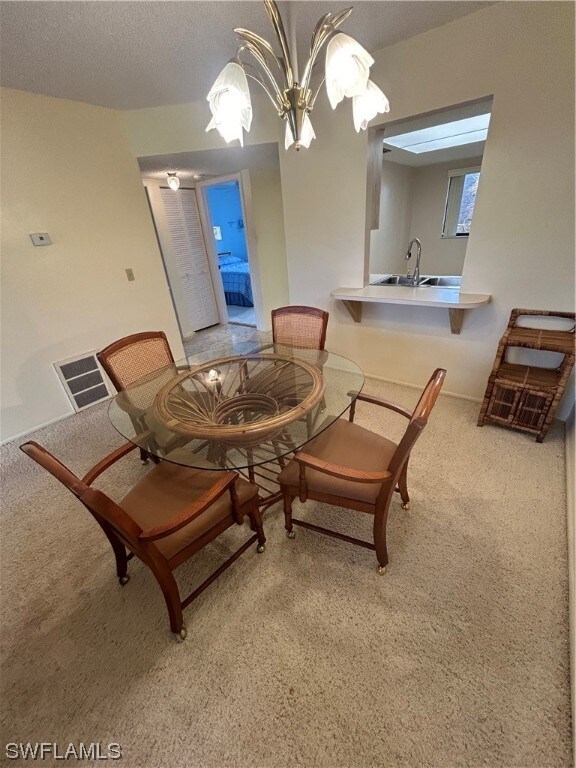 dining space with a chandelier, light carpet, a textured ceiling, and sink