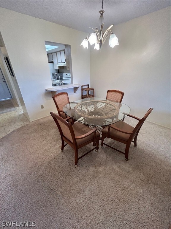 carpeted dining room featuring an inviting chandelier and a textured ceiling