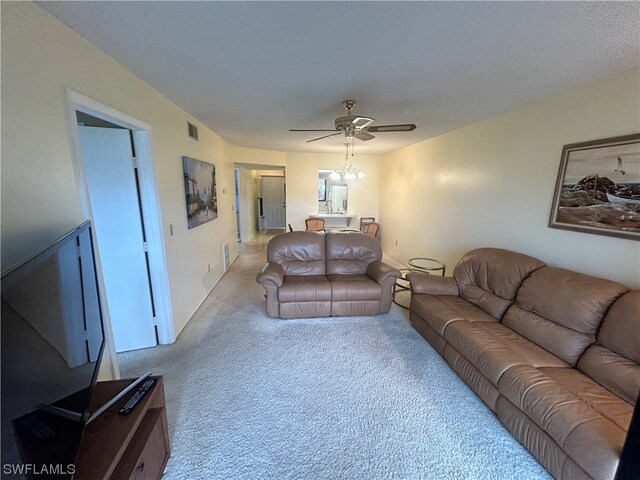 carpeted living room with ceiling fan with notable chandelier