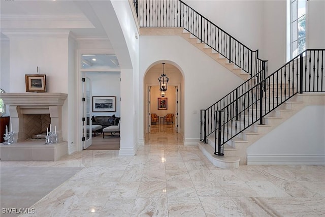 entrance foyer featuring baseboards, ornamental molding, a high ceiling, arched walkways, and marble finish floor