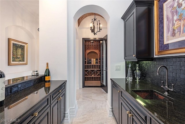 wine area featuring baseboards, wet bar, an inviting chandelier, marble finish floor, and a sink