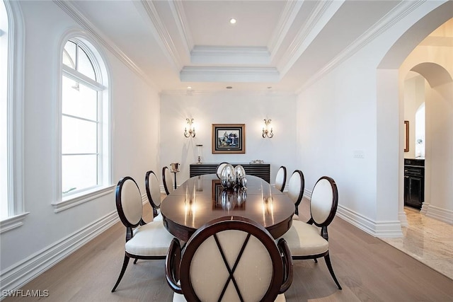 dining area with arched walkways, a tray ceiling, crown molding, and baseboards