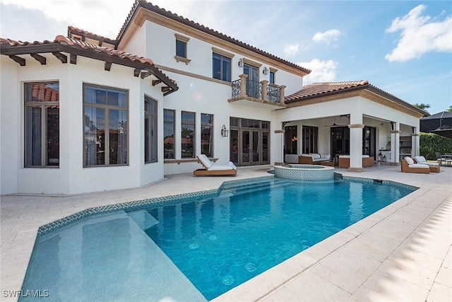 rear view of house featuring a pool with connected hot tub, stucco siding, french doors, a balcony, and a patio