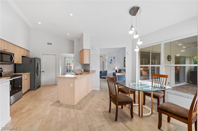 kitchen with light brown cabinetry, pendant lighting, sink, stainless steel appliances, and high vaulted ceiling