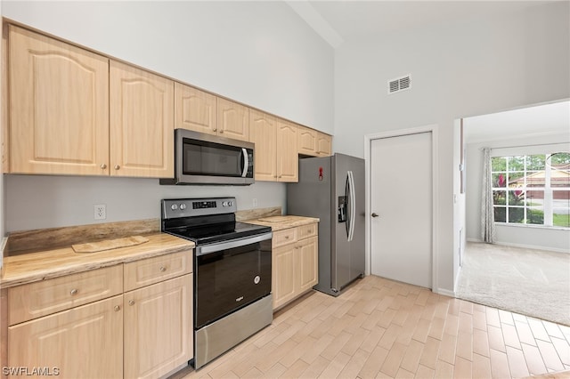 kitchen featuring light carpet, light brown cabinetry, stainless steel appliances, and a high ceiling