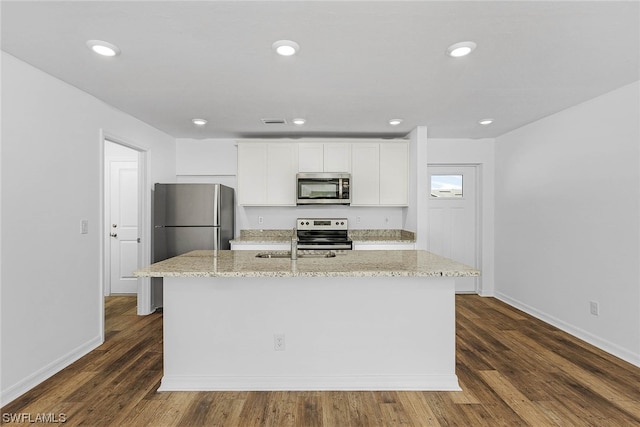 kitchen featuring dark hardwood / wood-style floors, a kitchen island with sink, light stone counters, appliances with stainless steel finishes, and white cabinetry