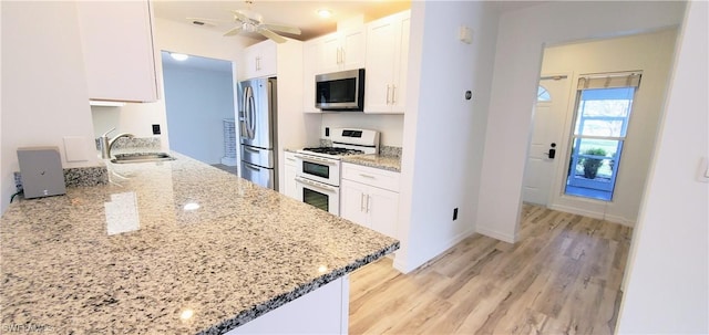 kitchen featuring sink, light stone counters, light wood-type flooring, stainless steel appliances, and white cabinets