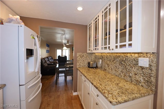 kitchen featuring light stone countertops, white fridge with ice dispenser, dark hardwood / wood-style floors, decorative backsplash, and white cabinets