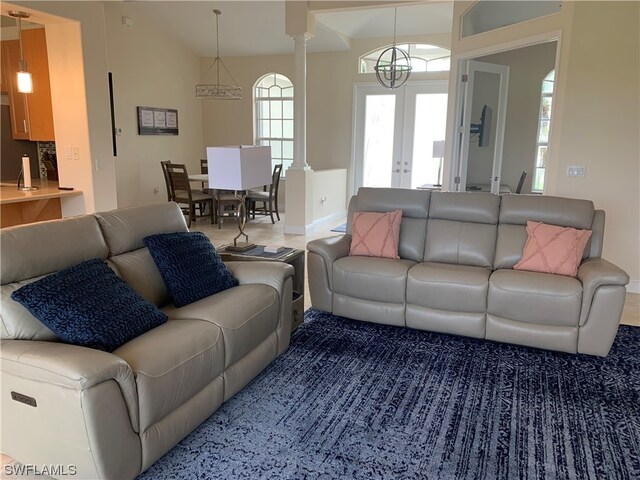 living room with a chandelier, decorative columns, high vaulted ceiling, and french doors