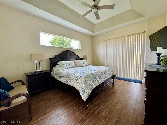 bedroom with dark hardwood / wood-style floors, ceiling fan, and a tray ceiling