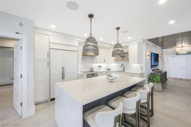 kitchen with paneled built in fridge, light tile floors, white cabinets, a center island, and pendant lighting