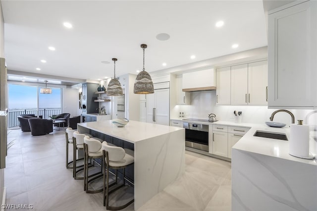 kitchen with decorative light fixtures, white cabinetry, sink, custom range hood, and stainless steel oven