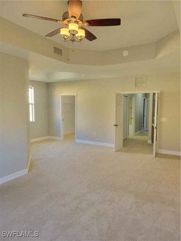 carpeted empty room with ceiling fan and a raised ceiling