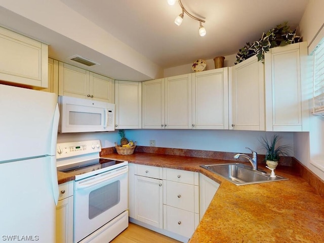 kitchen with white appliances, white cabinets, rail lighting, and sink