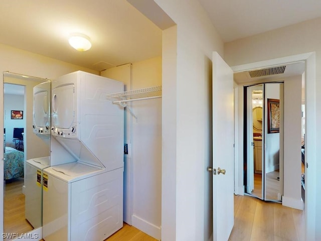 laundry area with stacked washer and clothes dryer and light hardwood / wood-style flooring