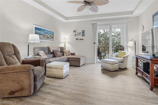 living area with ceiling fan, light wood-style flooring, baseboards, and a raised ceiling