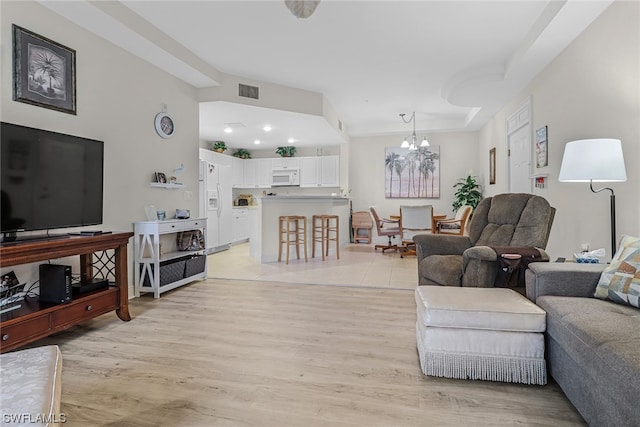 living room featuring light wood-type flooring, visible vents, and a notable chandelier