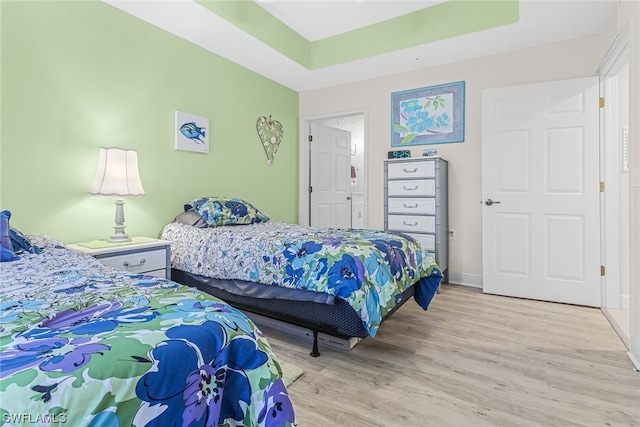 bedroom with light wood-style floors, a raised ceiling, and baseboards