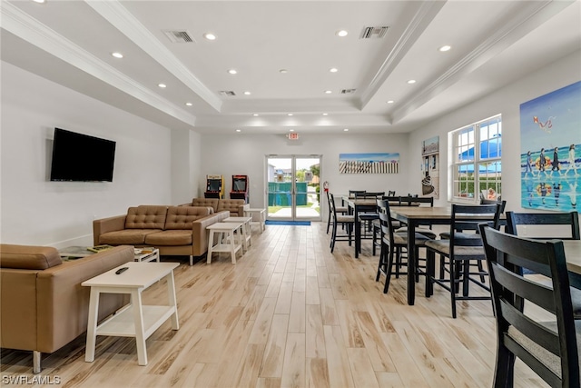 living room featuring light wood-style floors, a raised ceiling, visible vents, and ornamental molding